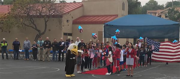 A photo of a young girl singing, as students line a red carpet, and military veterans sit nearby.